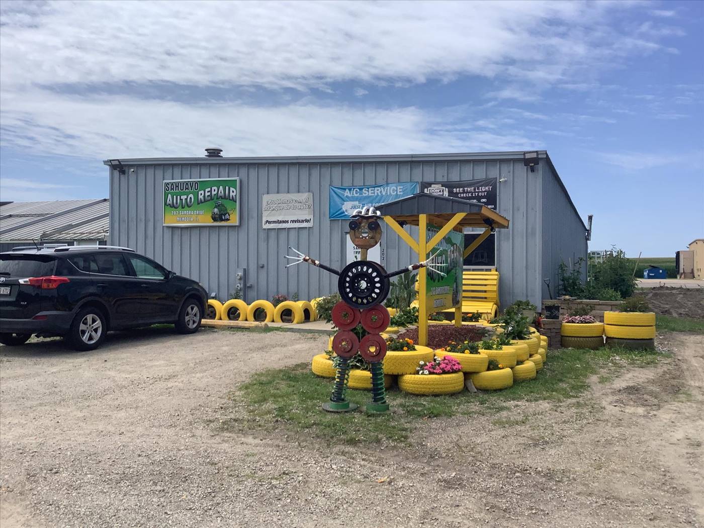 Gray metal shop building, bilingual yard sign, A/C banner, and tire sculpture at Sahuayo Auto Repair